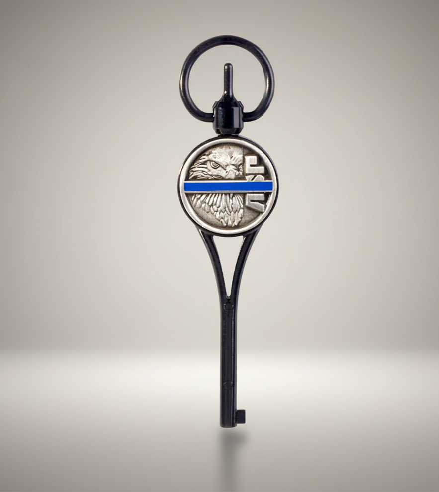 Key-shaped keychain with an eagle emblem and thin blue line on a beige background