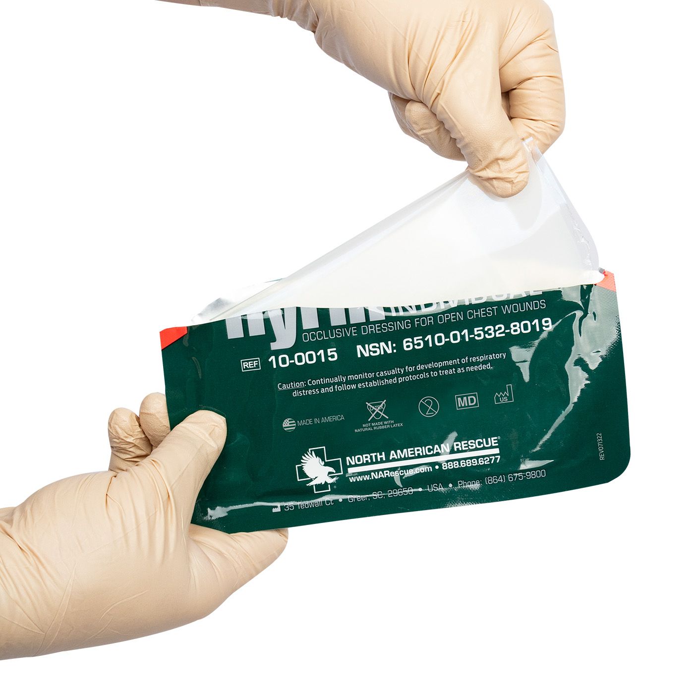 Hand wearing a glove holding a green medical dressing package with text on a white background