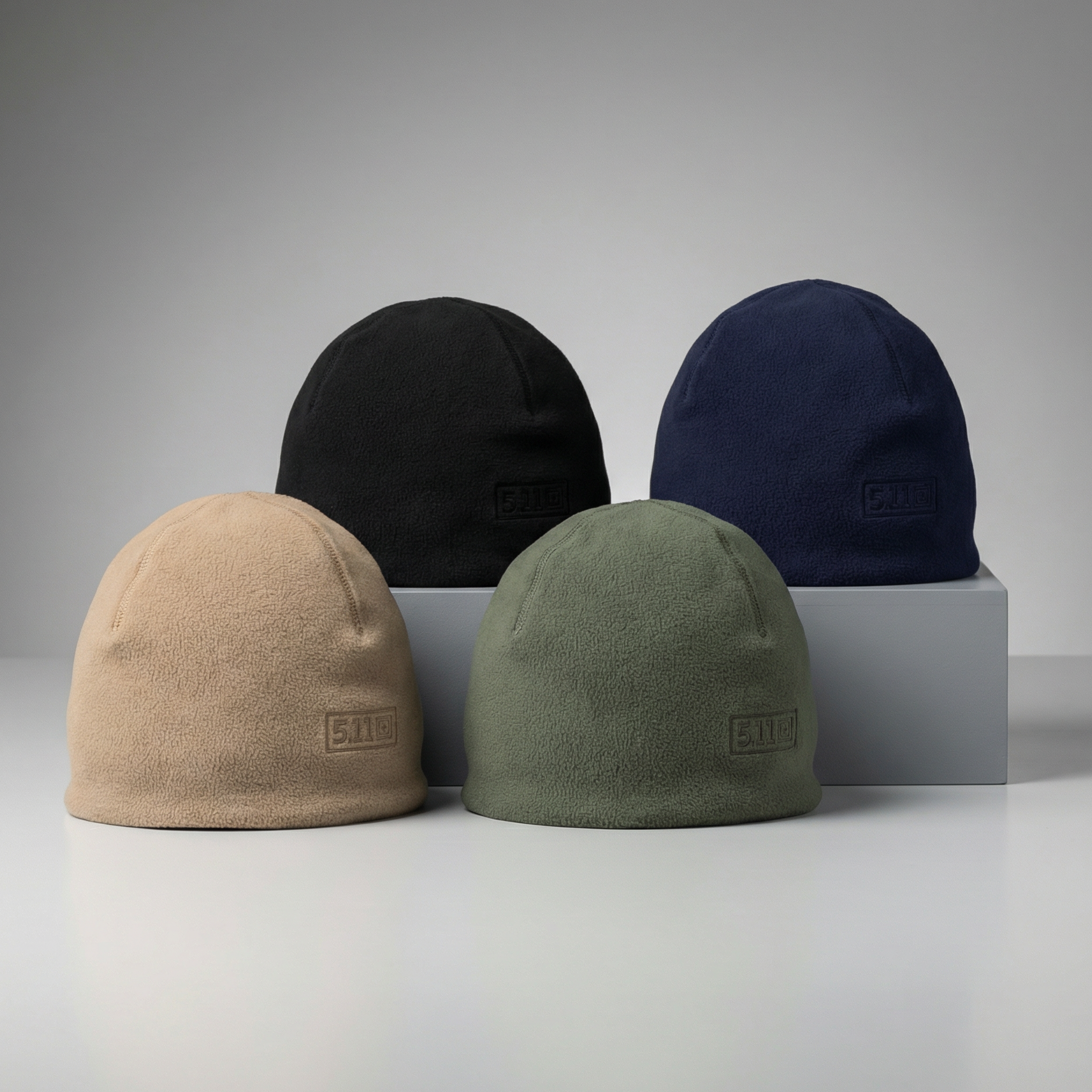Four beanies in beige, black, green, and navy on a gray background
