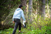 Woman hiking through a forest while carrying camping gear and a folding shovel, enjoying outdoor exploration.