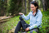 Woman happily unfolds the Gerber Gear Gorge Folding Shovel in a lush forest, showcasing its portability and ease of use.