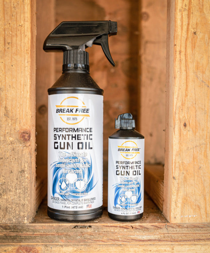 Two bottles of Break Free Performance Synthetic Gun Oil on a wooden shelf.