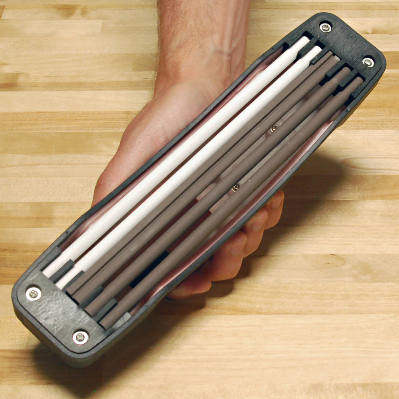 Bottom view of the Lansky Master's Edge MEDGE1 held in hand, showing all five ceramic rods loaded into the molded snap-in storage slots on the underside of the base