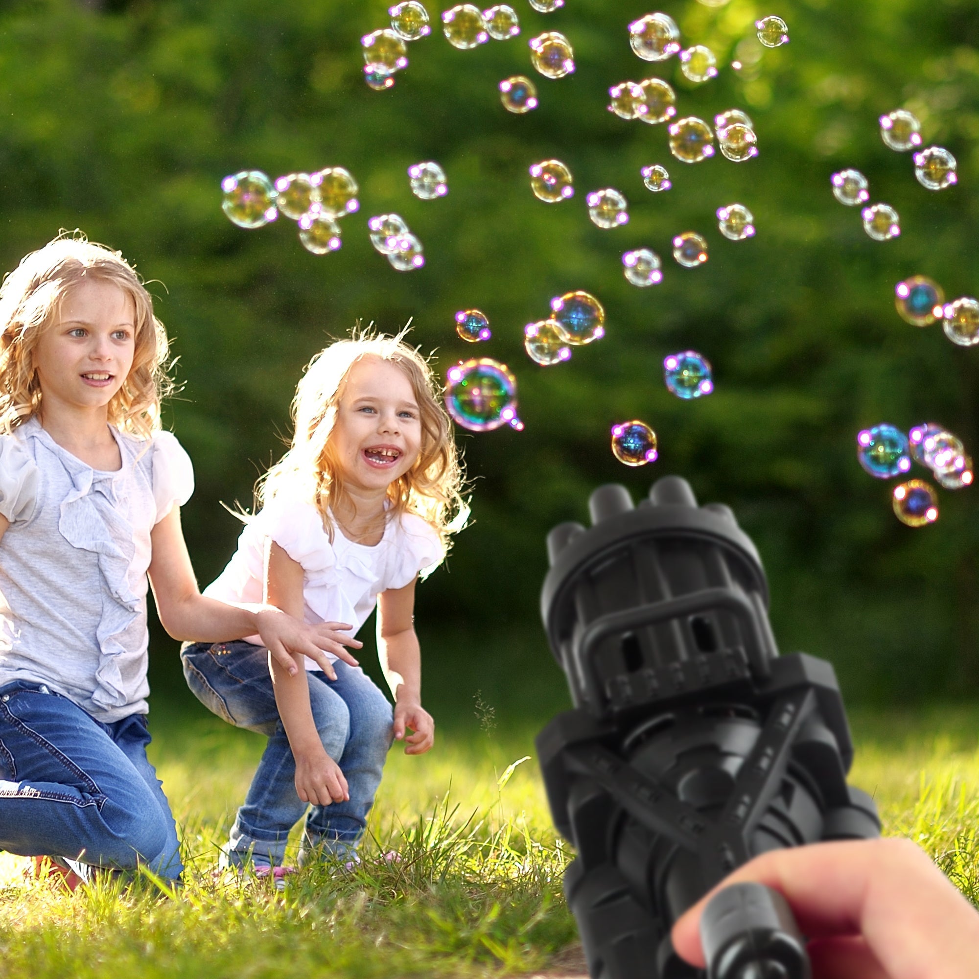 Two children playing with a bubble gun in a grassy area with bubbles floating around.