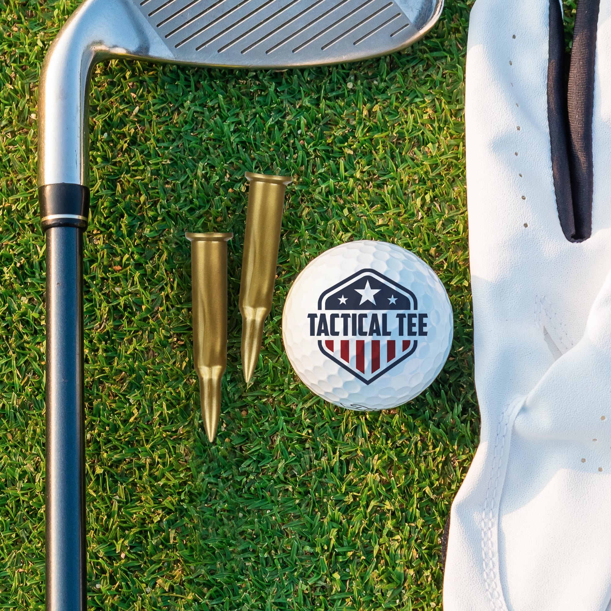 Golf club, gold bullets, and a golf ball with 'Tactical Tee' logo on grass