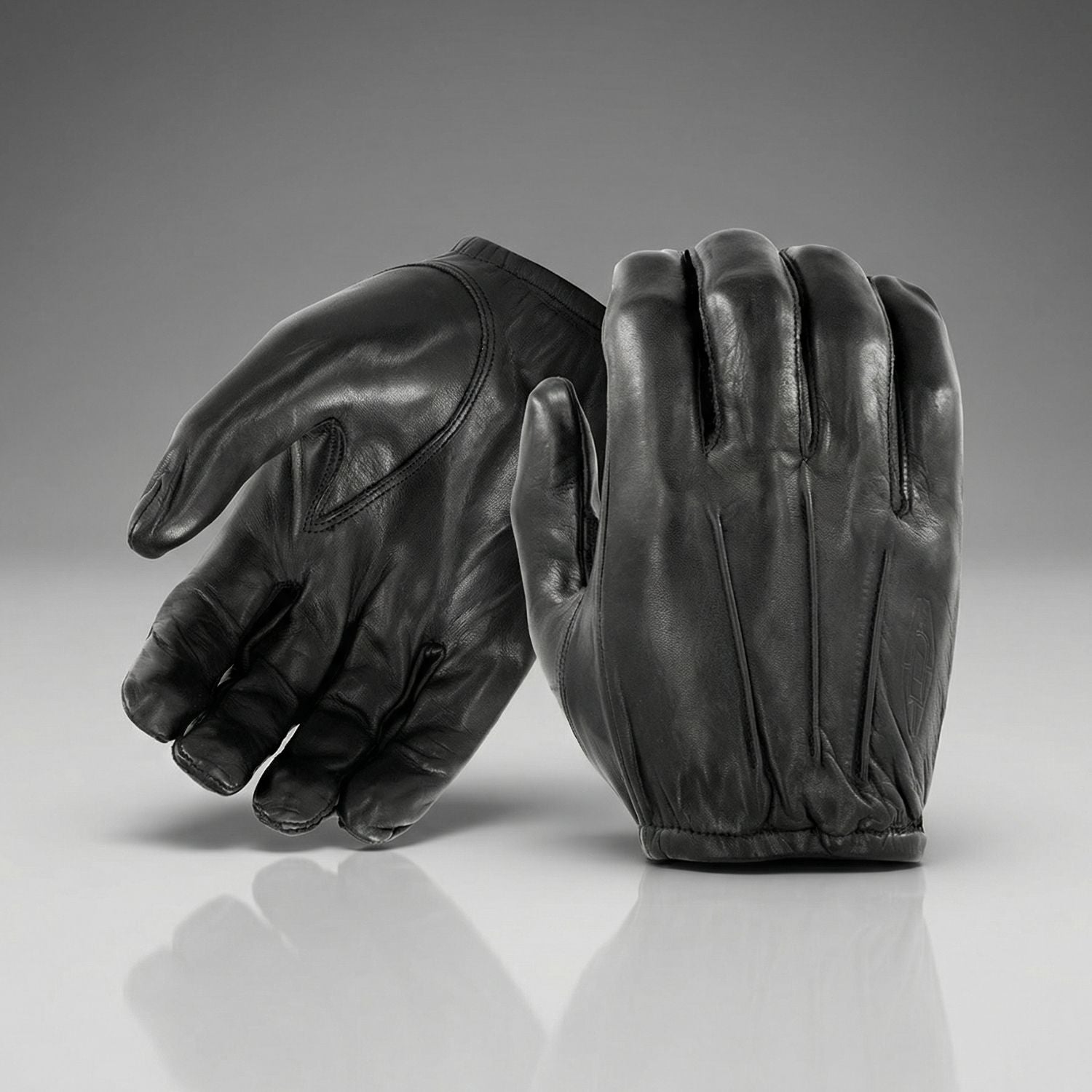Pair of black leather gloves on a reflective surface with a gray background