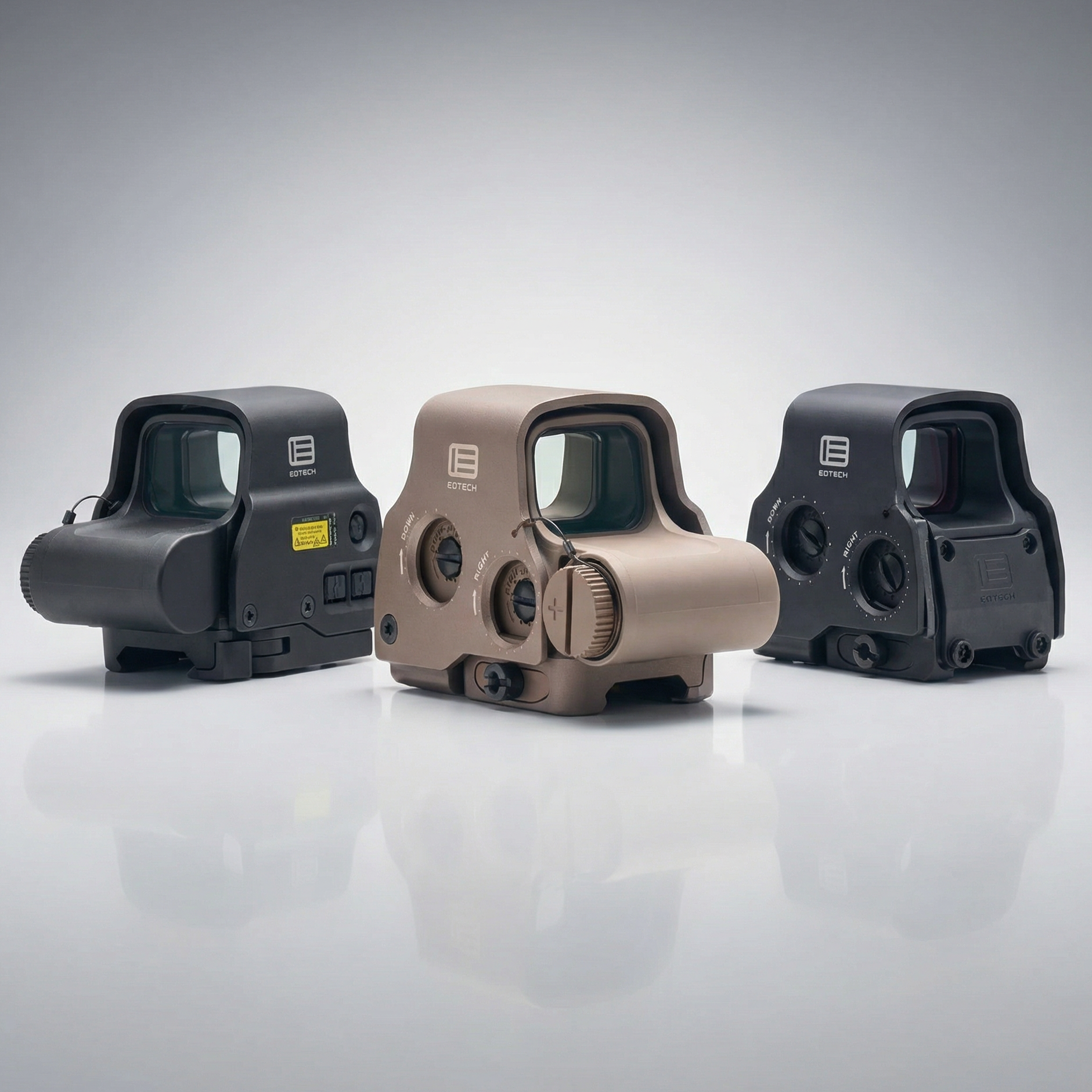 Three tactical sight devices on a reflective gray surface with a light gray background