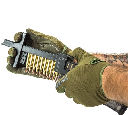 Hand holding a magazine loader with ammunition, wearing green gloves on a white background