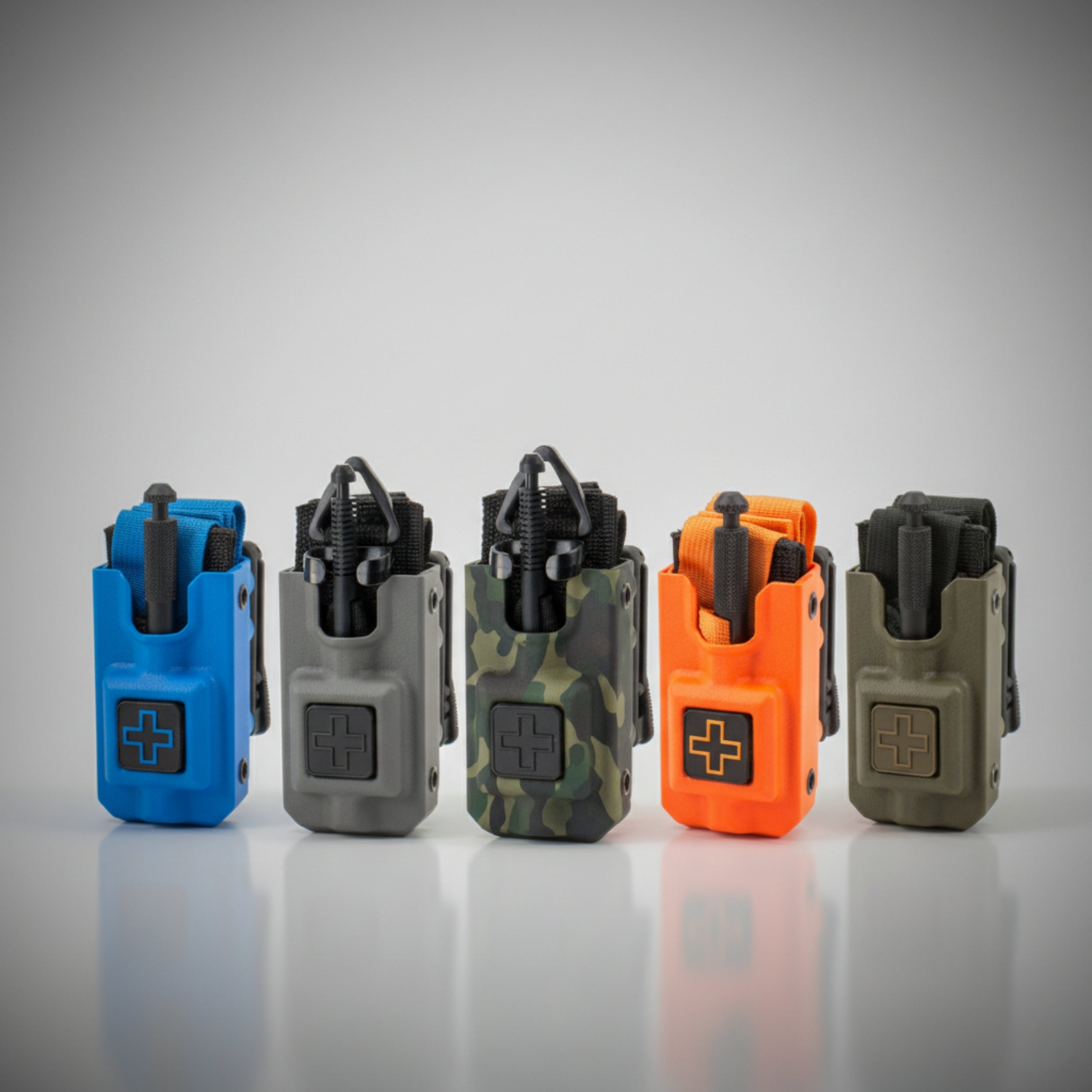 Five Eleven 10 RIGID Tourniquet Cases for SOFTT/SOFTT-W in blue, gray, camouflage, orange, and green on a reflective surface with a gray background.