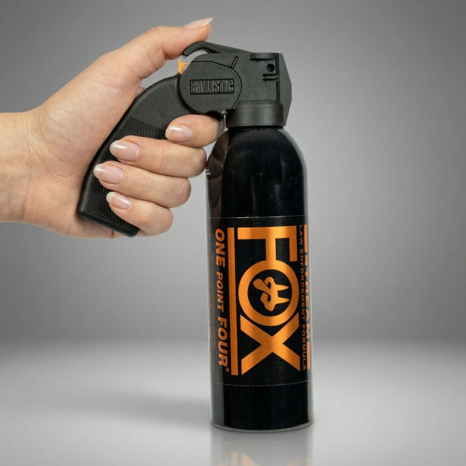Hand holding a black pepper spray canister with 'FOX' branding on a gray background