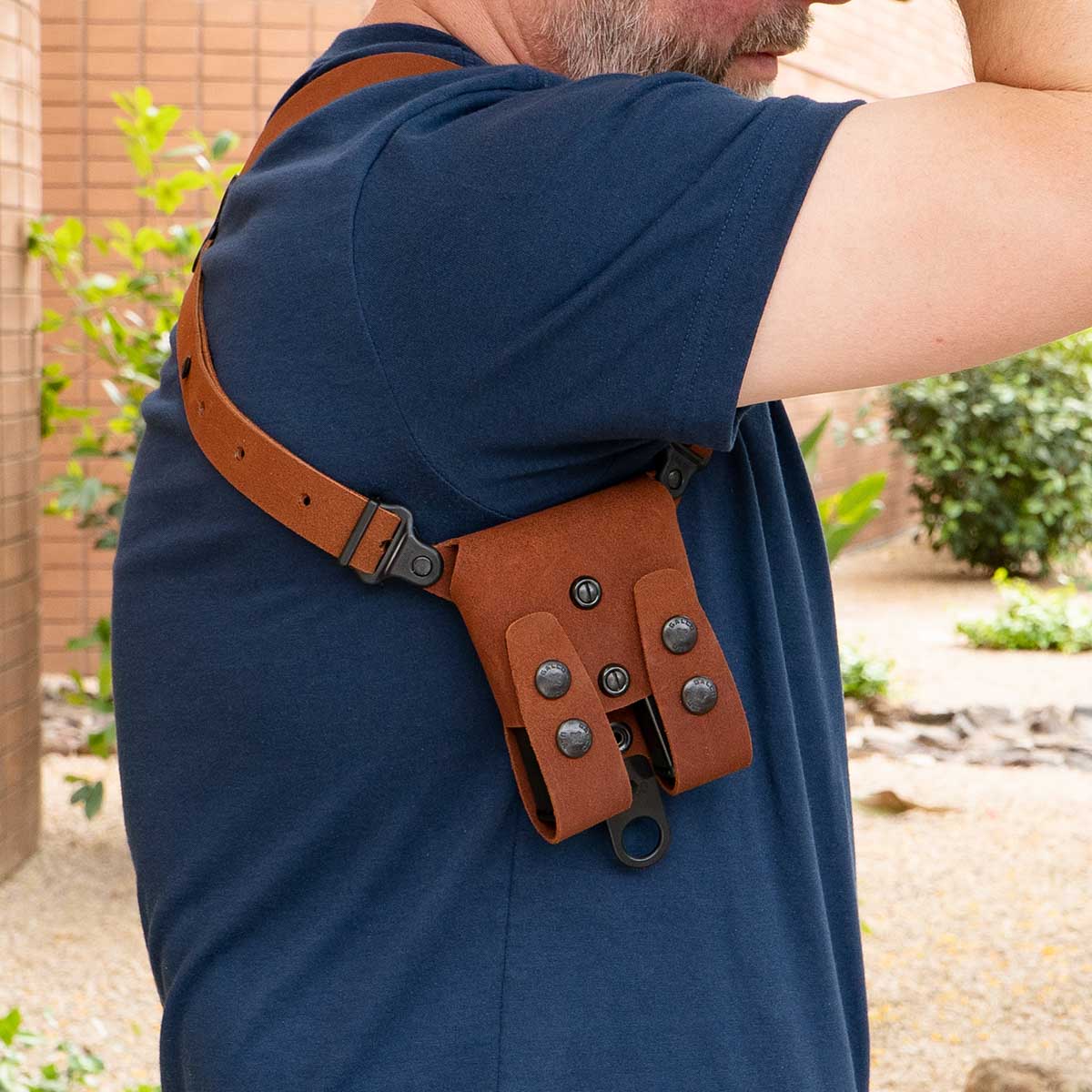 Person wearing a brown leather holster on their shoulder outdoors.