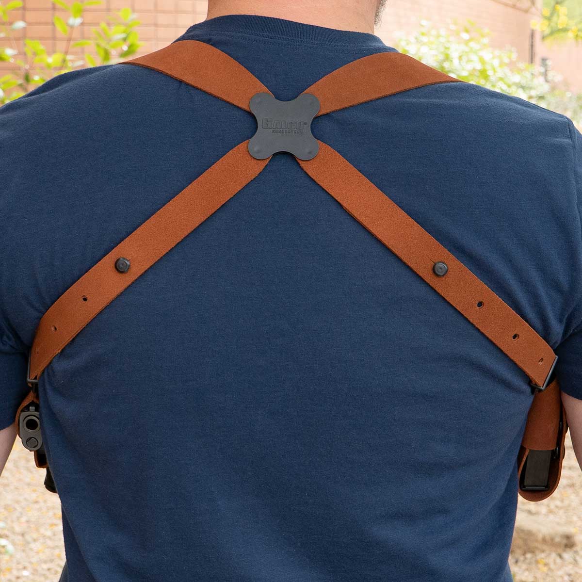 Person wearing brown leather shoulder holster over a blue shirt with a blurred outdoor background