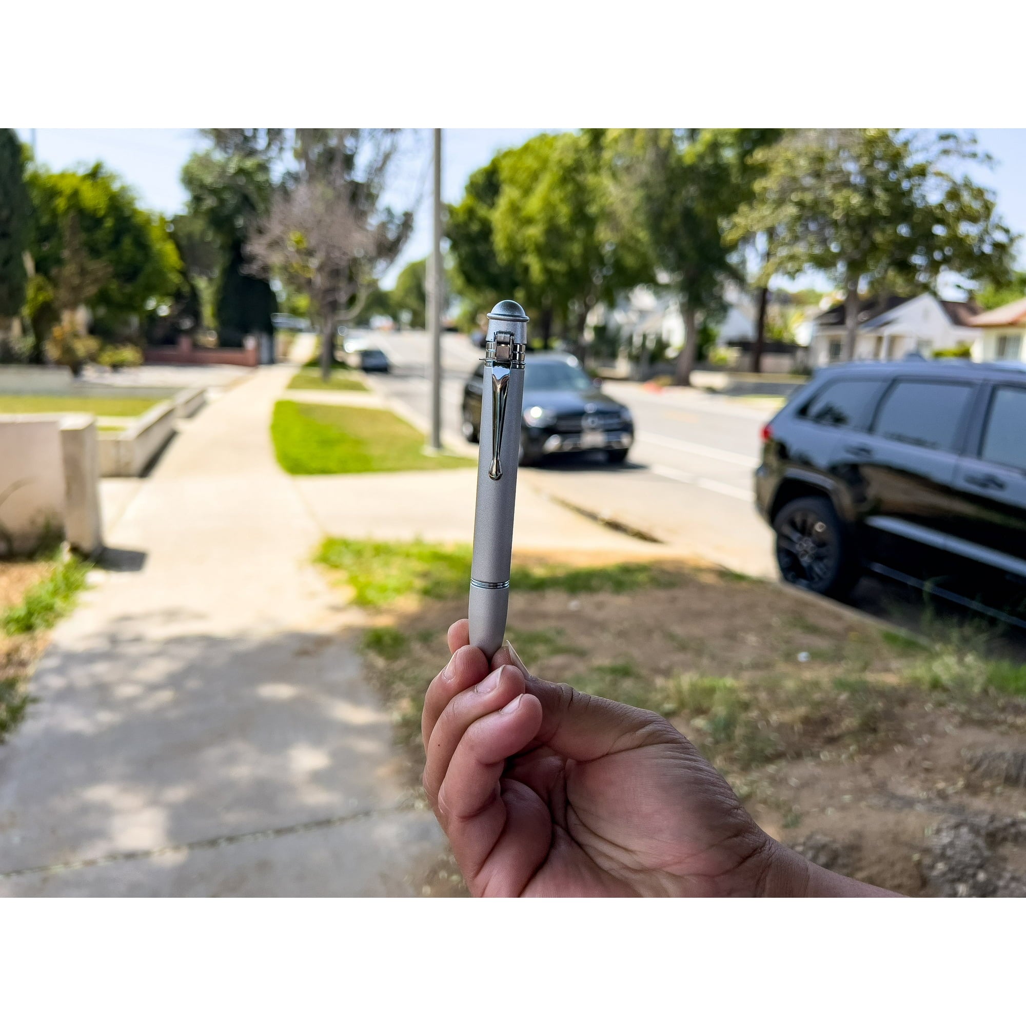 Hand holding a pepper spray pen with a blurred street scene in the background