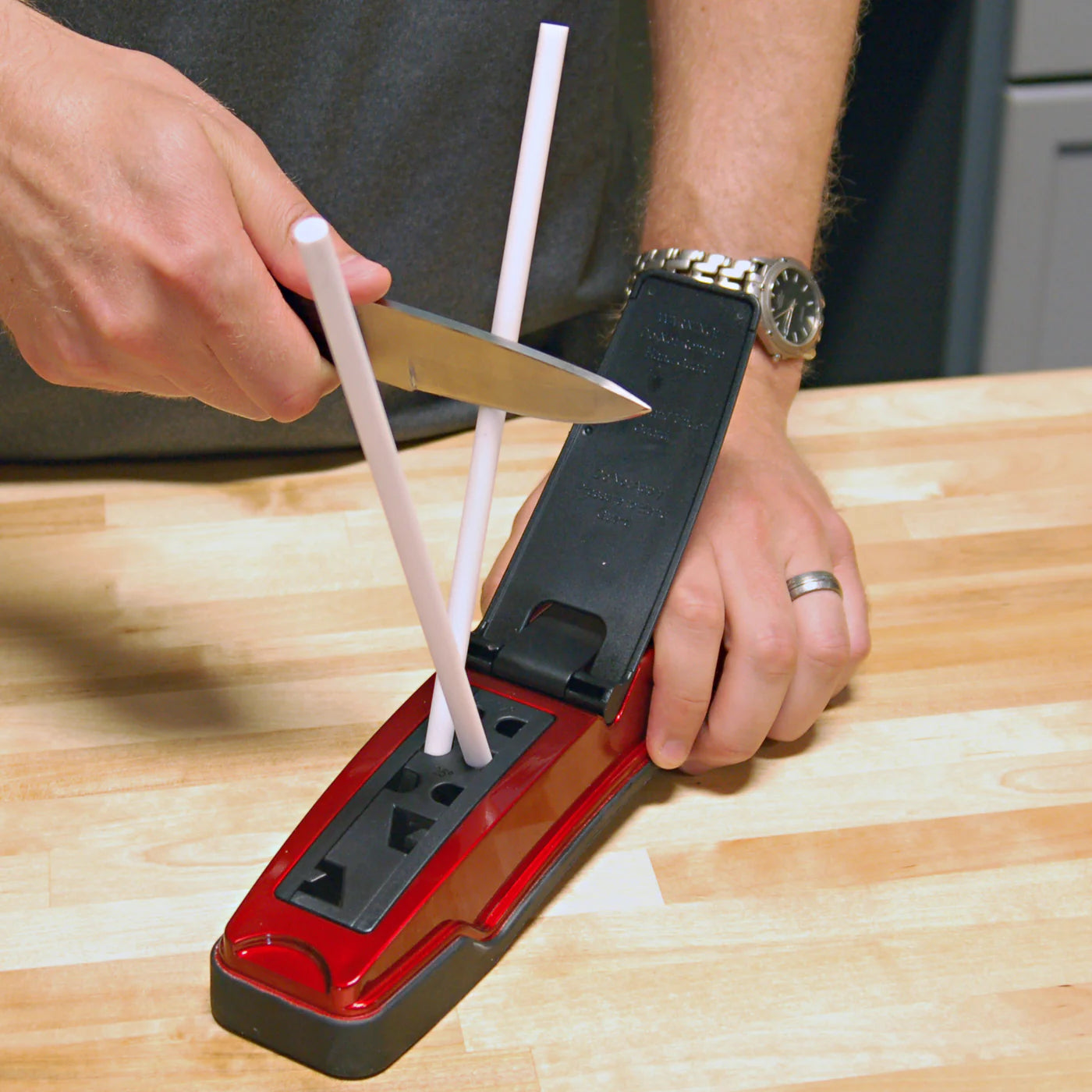 Lansky Master's Edge knife sharpening system model MEDGE1 in use, sharpening a kitchen knife on a butcher block counter using white fine ceramic rods
