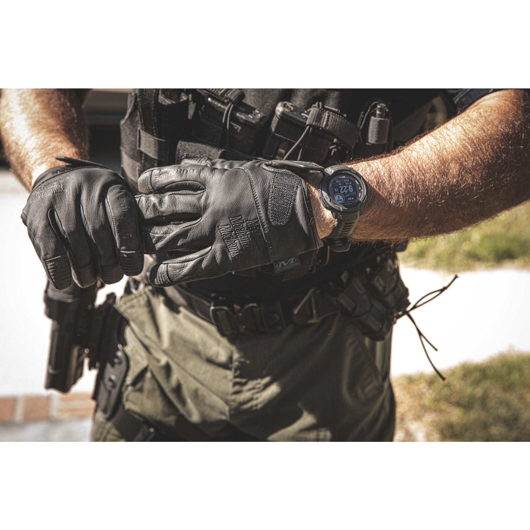 Person wearing tactical gloves and a watch, with a gun holster, in an outdoor setting.
