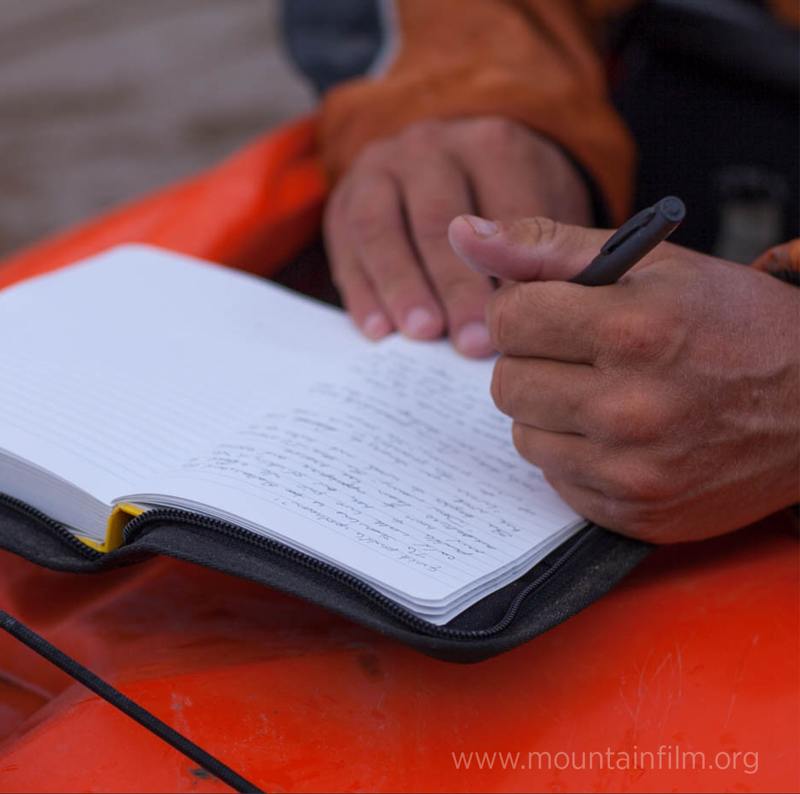 Person writing in a notebook on a red kayak