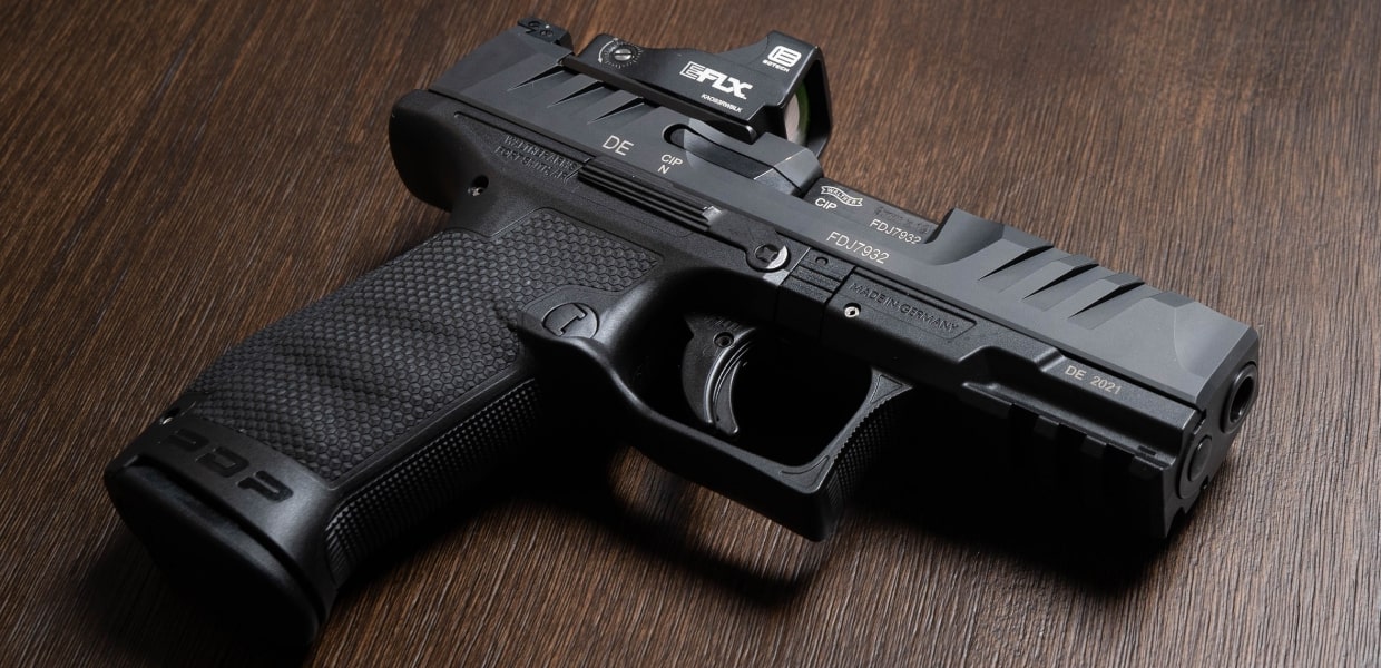 Black handgun with EOTech EFLX mini red dot sight mounted on top against a wooden background.