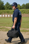 Man in police uniform carrying a bag on a training range