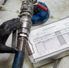 Hand holding a mechanical component next to a Daily Def Driver Report form.