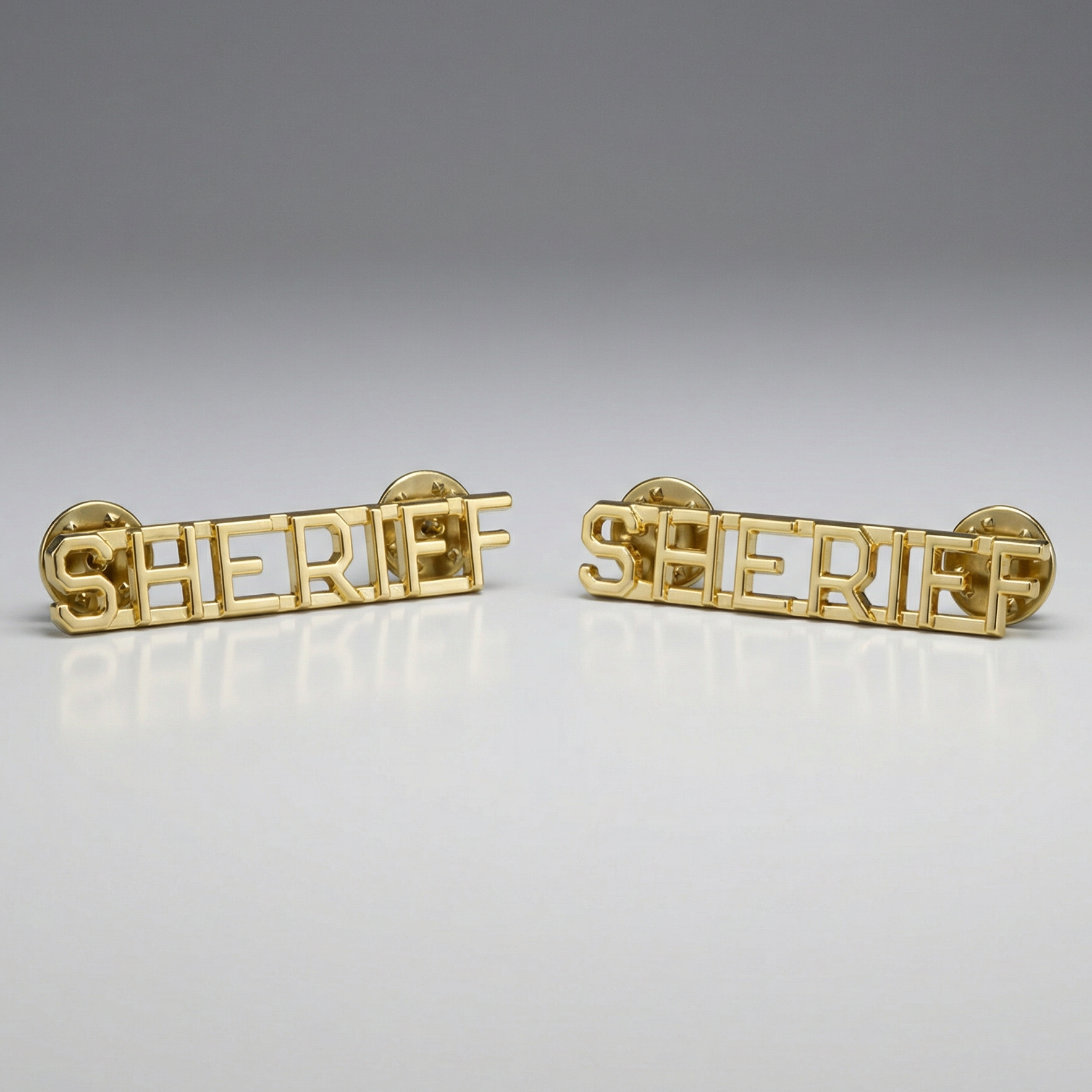 Two gold 'SHERIFF' pins on a gray background