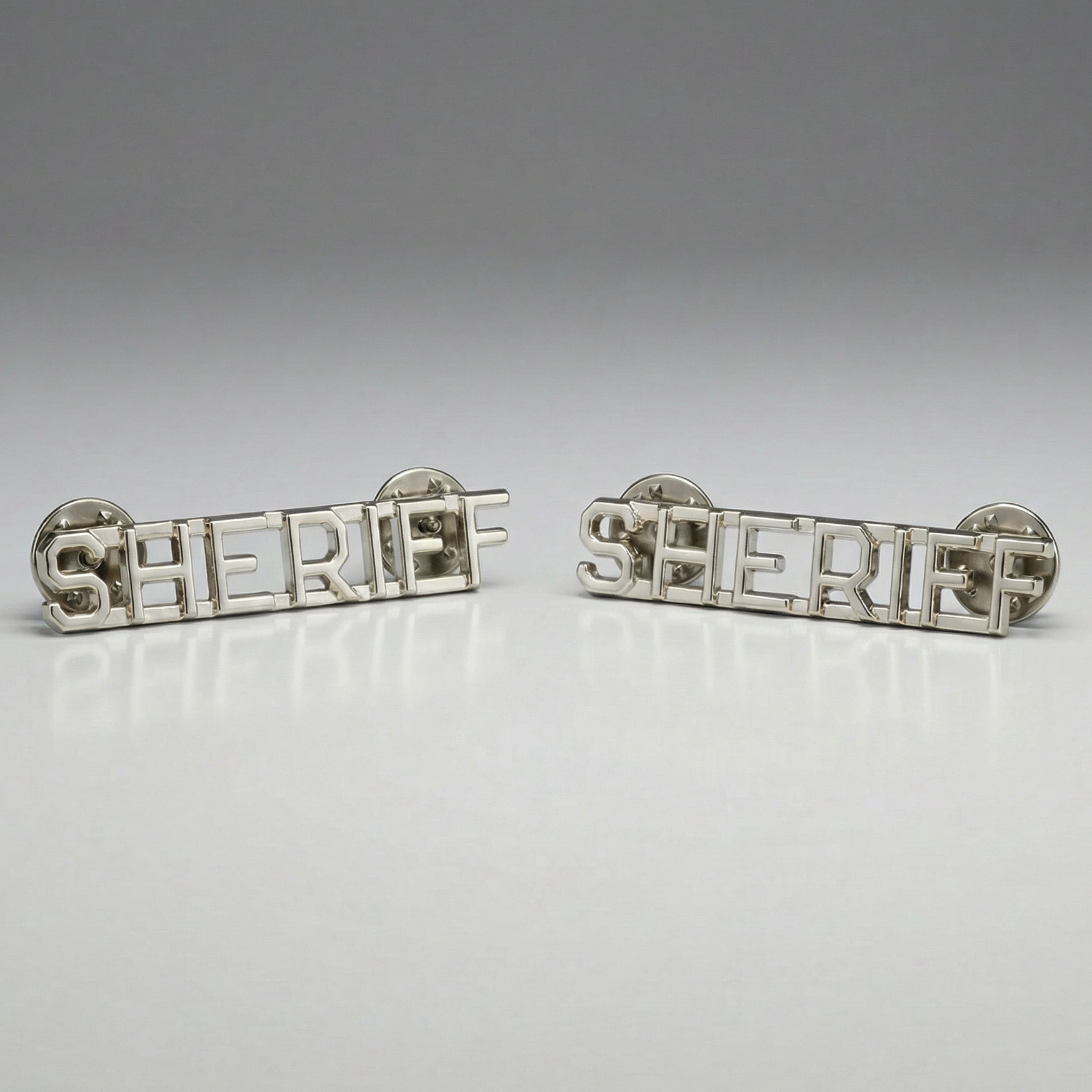 Pair of silver 'SHERIFF' pins on a gray background
