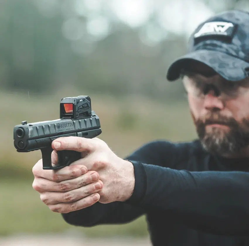 Person holding a handgun with a blurred natural background