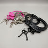 Set of handcuffs in black, pink, and silver with keys on a gray background