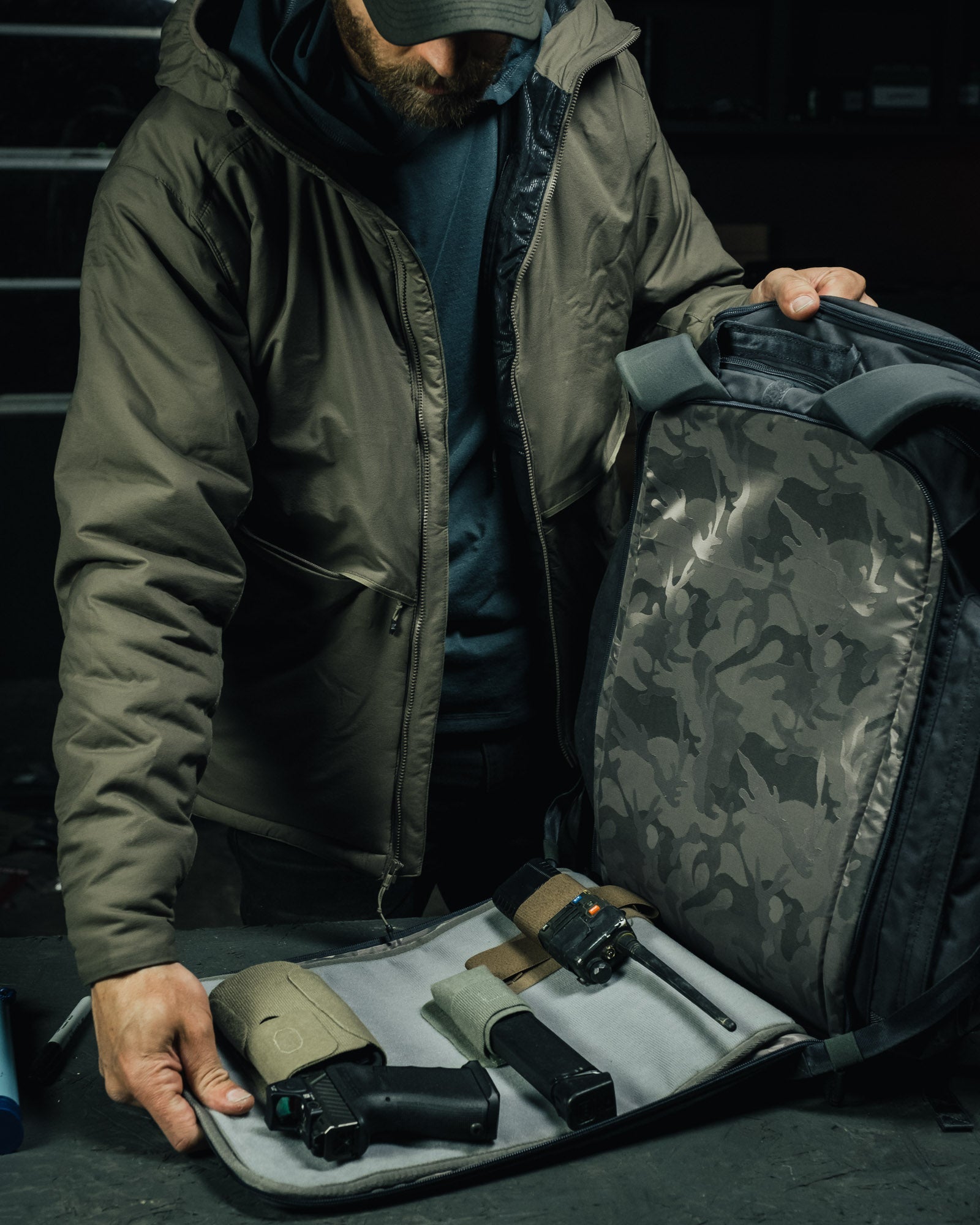 Person in a green jacket with a camouflage backpack, holding a handgun and ammunition.