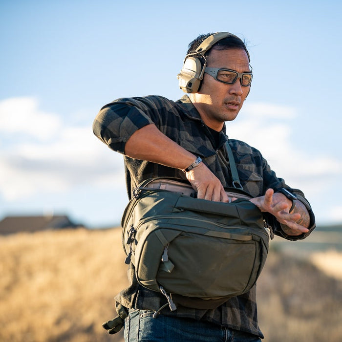 Man wearing a green backpack outdoors with a clear sky background