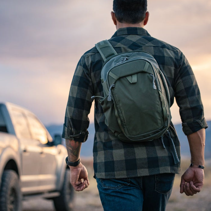 Man with a green backpack walking away from a vehicle towards a scenic landscape.