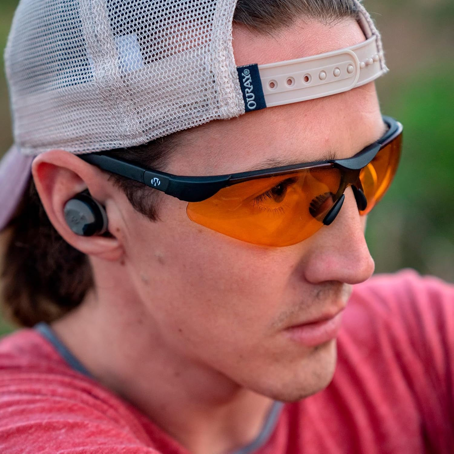 Person wearing orange-tinted sunglasses and a white cap with a brand logo.