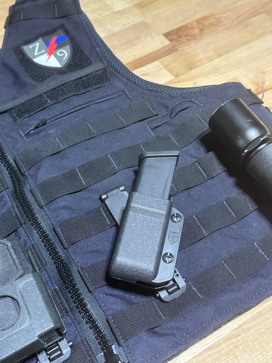 Black tactical vest with gun holster and visible branding on a wooden surface