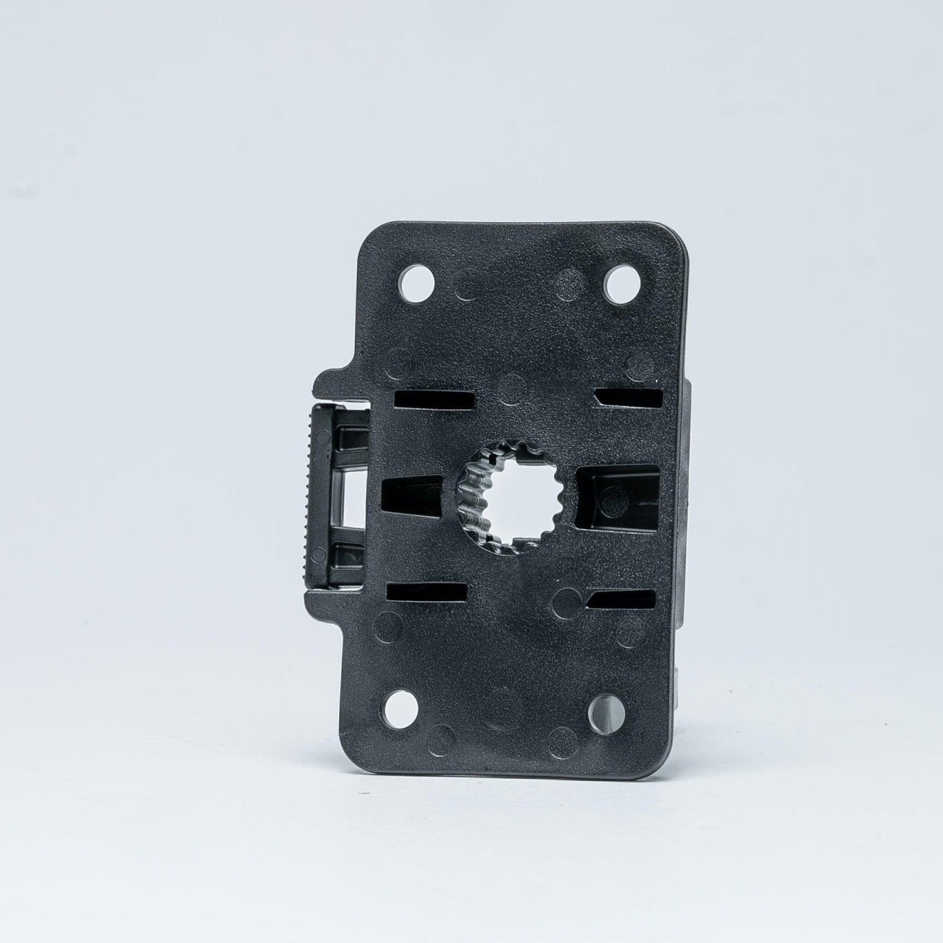 A black plastic mounting bracket or adapter with four pre-drilled screw holes and a central gear-shaped cutout, shown on a light gray studio background.