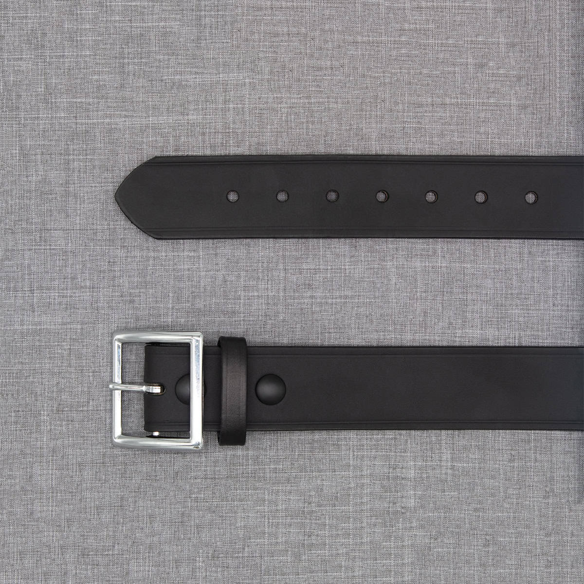 Black leather belt with silver buckle on a gray fabric background