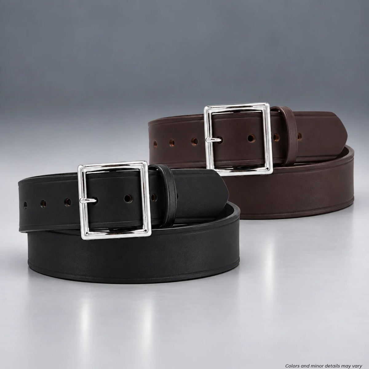Two leather belts, one black and one dark brown, coiled on a reflective gray surface with a gray gradient background. Each belt has a polished silver-tone square buckle.