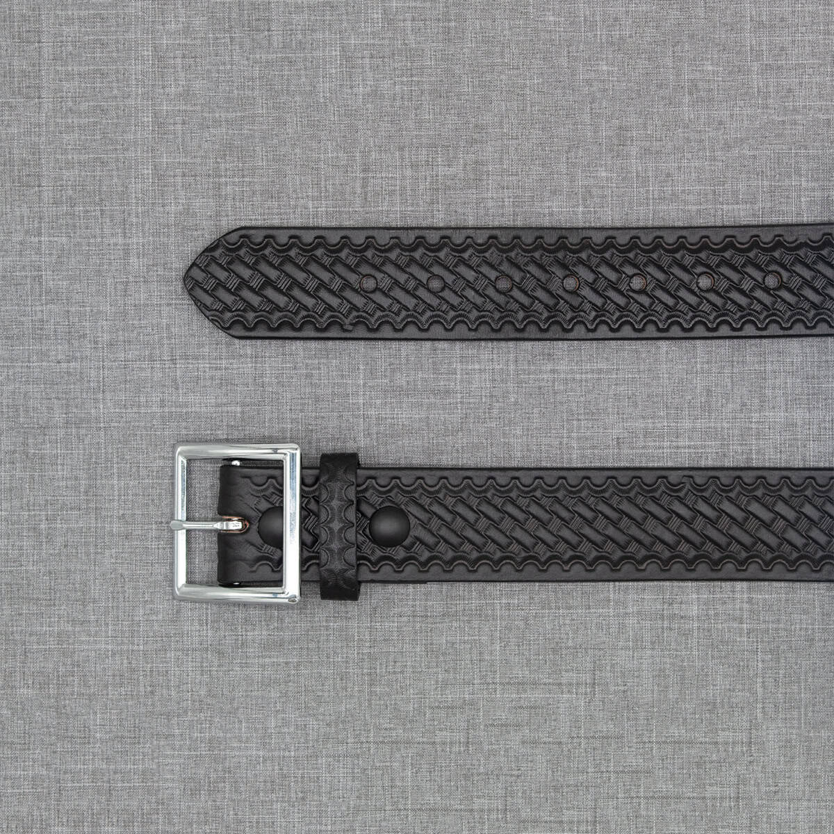A black woven leather watch strap with a silver metal buckle, laid flat on a textured gray background.