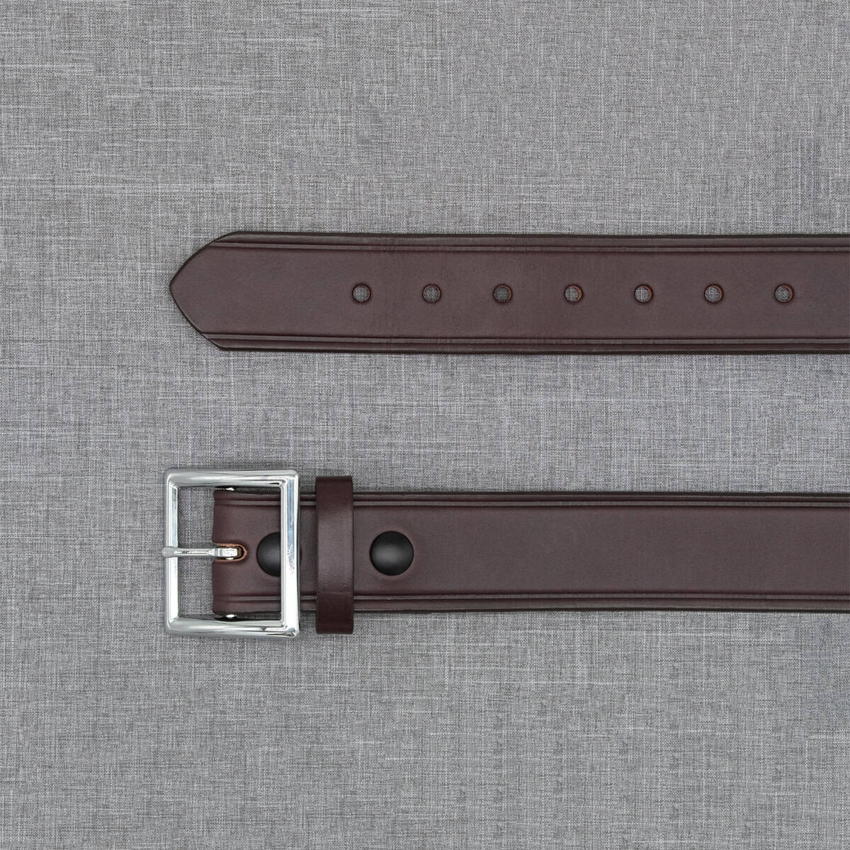 A dark brown leather belt with a silver-tone metal buckle, laid flat on a textured gray fabric background.