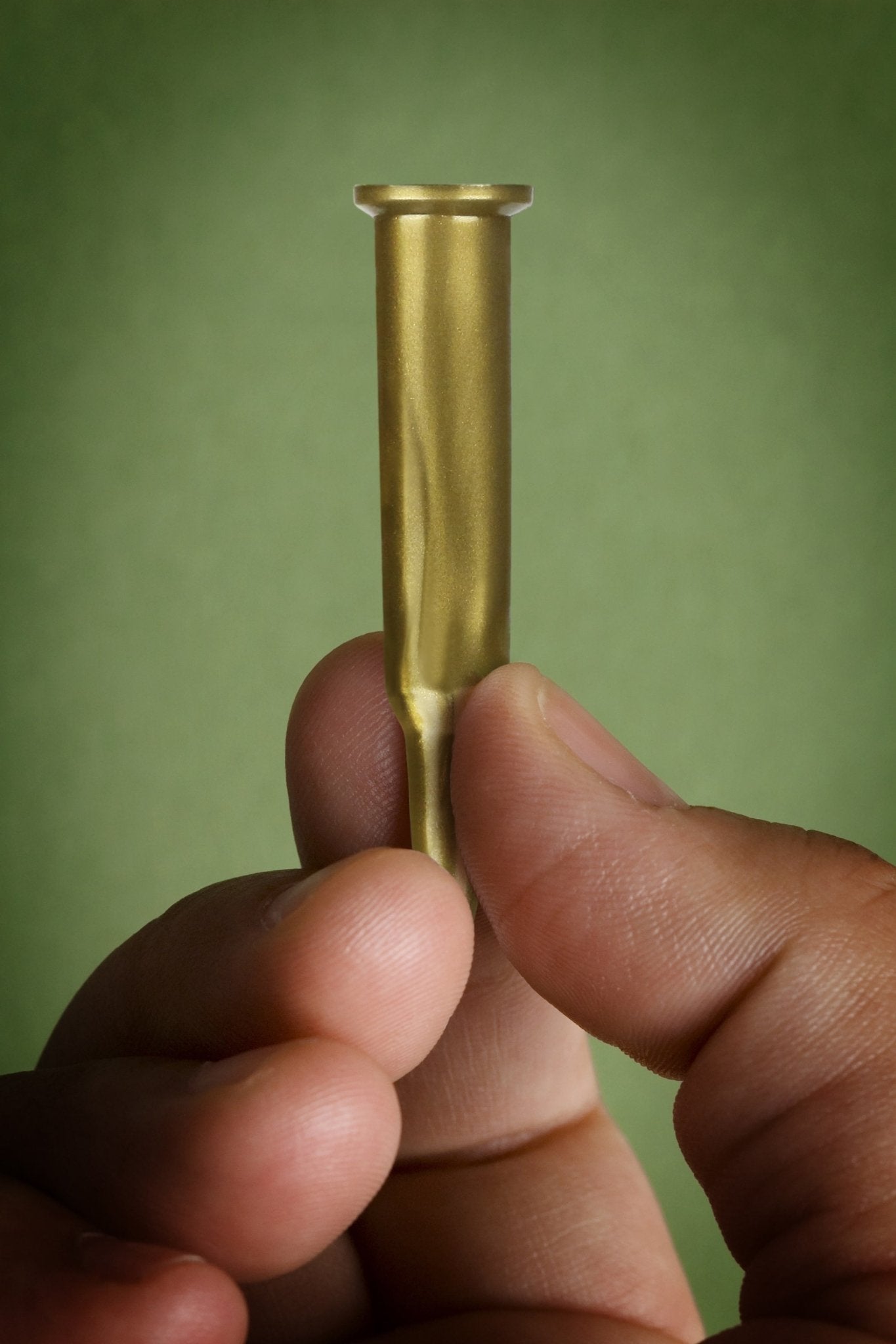 Hand holding a brass bullet casing against a green background