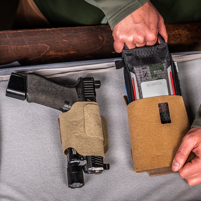 Person holding a rifle with attached magazine and pouches on a gray surface