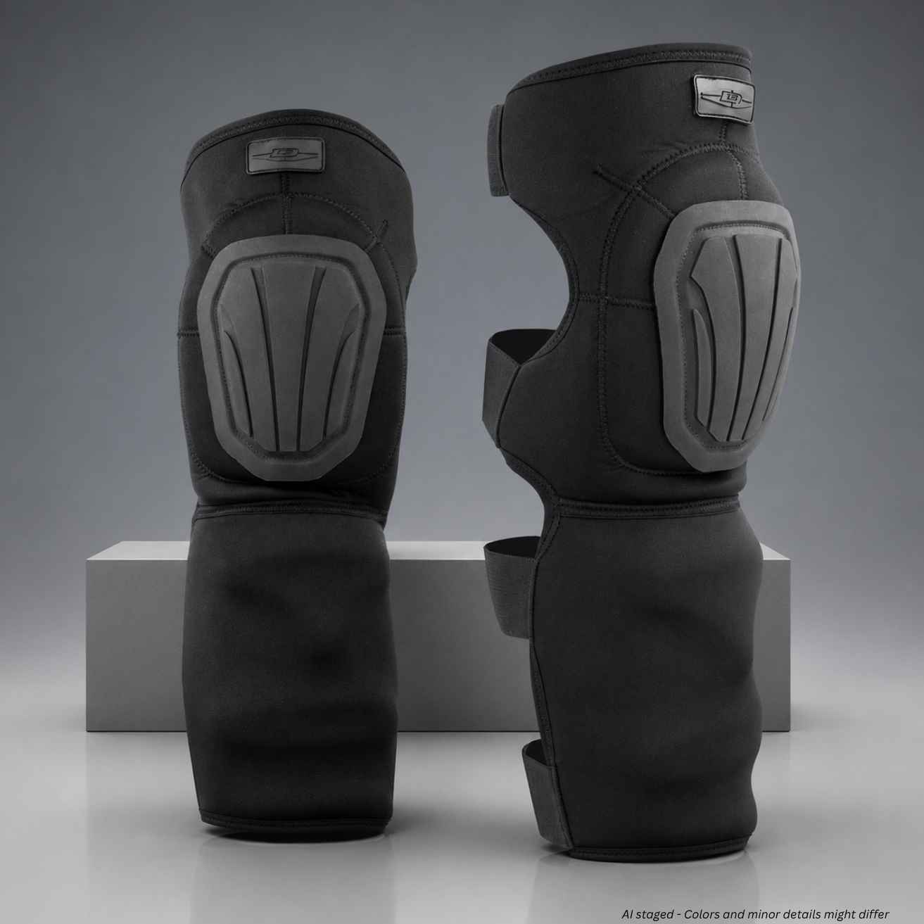 A pair of black protective shin guards with gray molded shin and knee pads, displayed on a gray studio background with a white block.