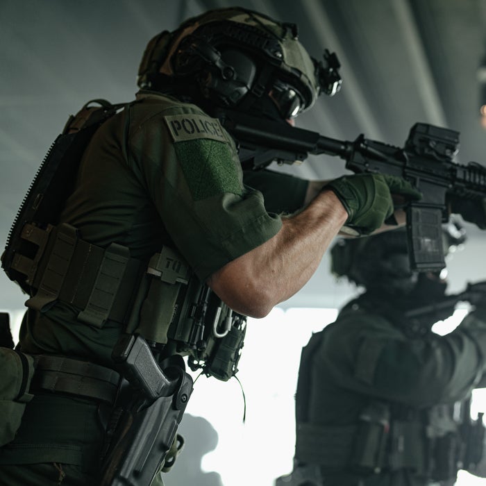 Tactical police officer in combat gear aiming weapon during operations in low-light conditions.