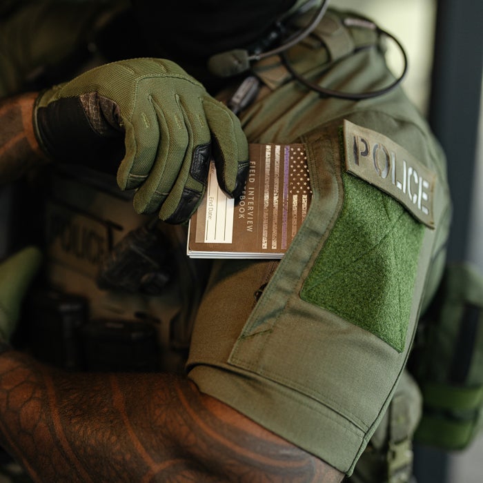 Tactical police officer in OD green uniform holding a tactical booklet, showcasing combat-ready gear and functionality.