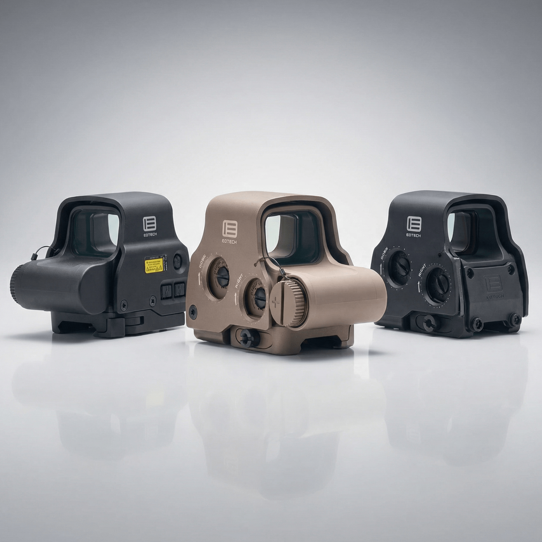 Three tactical sight devices on a reflective gray surface with a light gray background