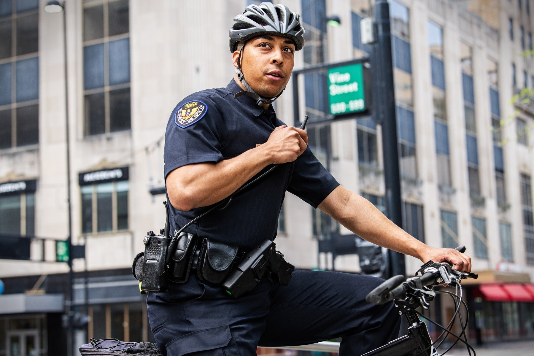 Police officer in Flying Cross FX STAT Hybrid Shirt riding a bicycle on duty, using a radio