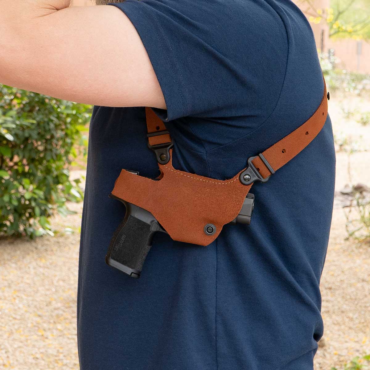 Person wearing a brown leather gun holster on a blue shirt outdoors.