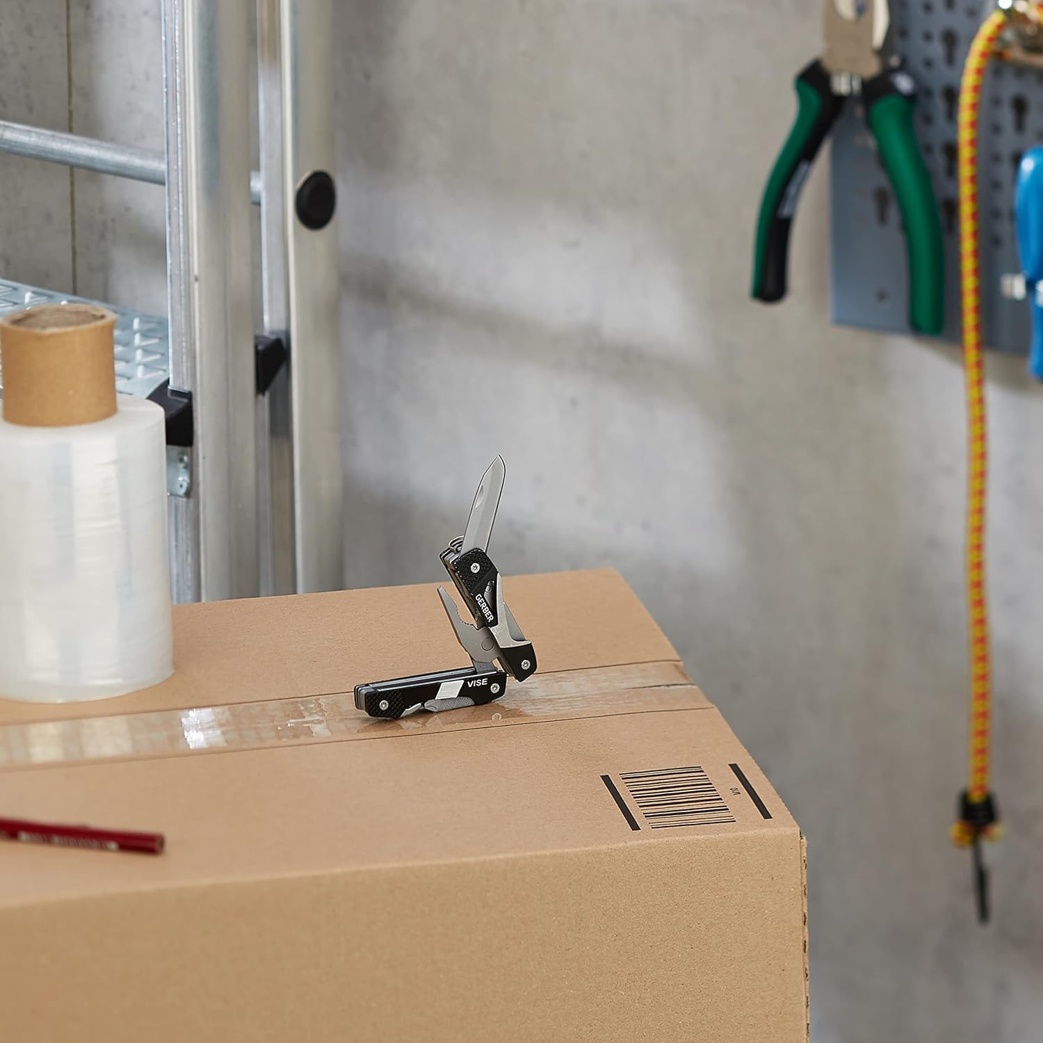 Cardboard box with a knife on top, in a workshop setting with tools in the background.