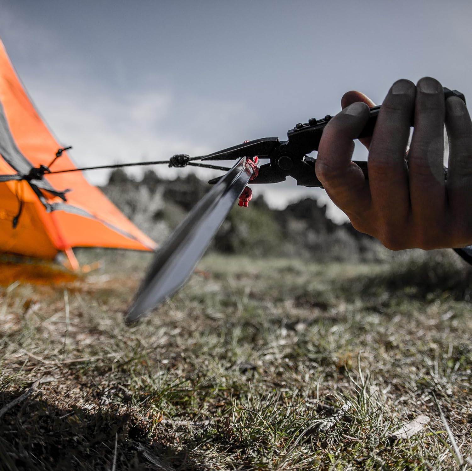 Black Gerber Multi-Plier 600 needlenose pliers gripping a tent stake and guy line at camp