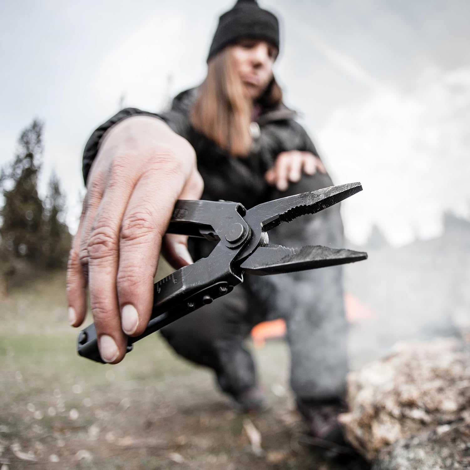 Camper holding a black Gerber Multi-Plier 600 Needlenose with jaws open beside a campfire