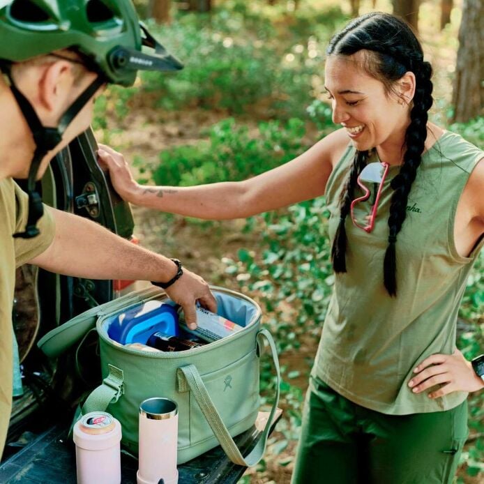 Two people happily unpacking a Hydro Flask cooler in a forested outdoor setting.