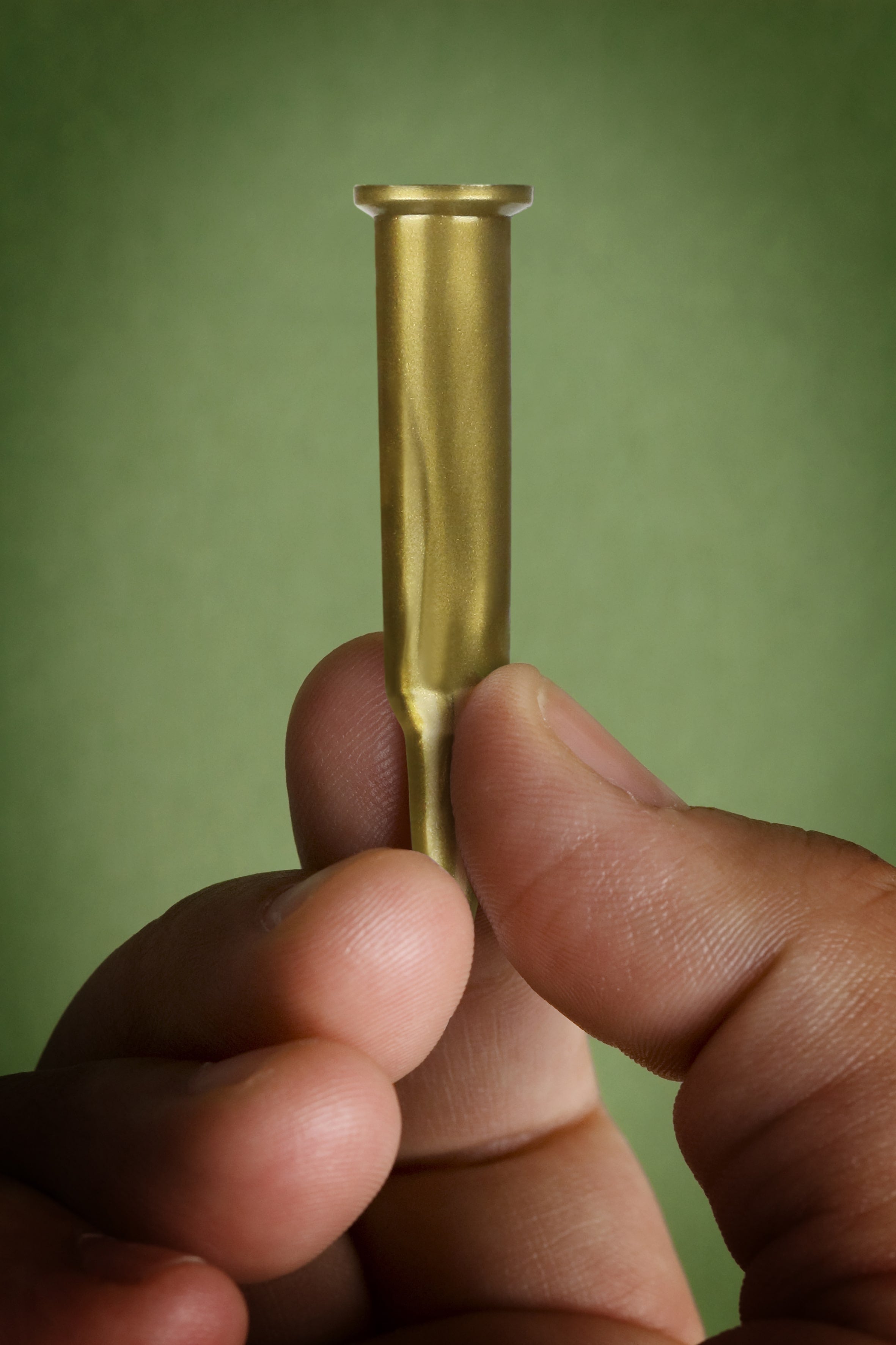 Hand holding a brass bullet casing against a green background